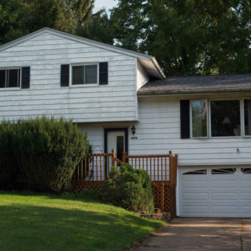 A split-level house with peeling paint on the aluminum siding and overgrown bushes in front